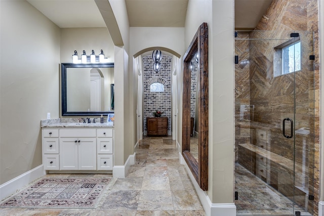 bathroom featuring vanity, a shower stall, baseboards, and stone finish flooring