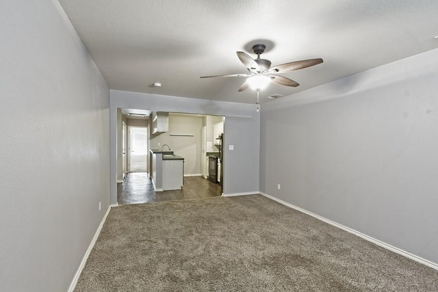 unfurnished living room featuring visible vents, baseboards, a sink, ceiling fan, and dark colored carpet