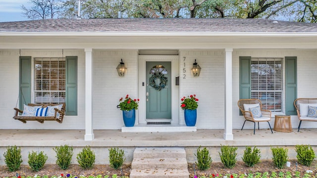 view of exterior entry featuring brick siding, a porch, and a shingled roof