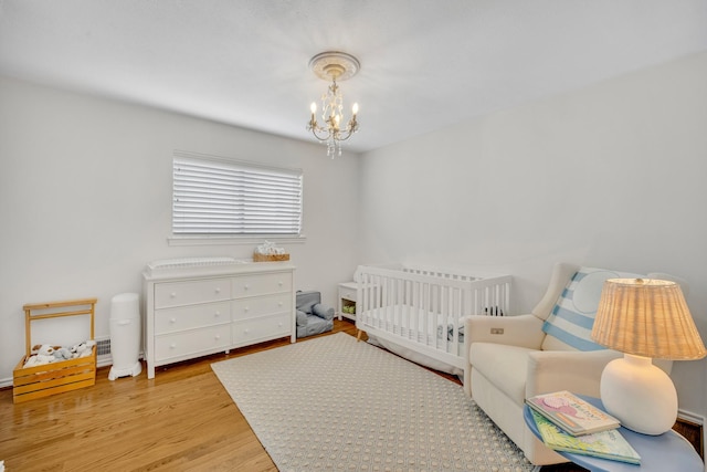 bedroom with a notable chandelier, a nursery area, and wood finished floors