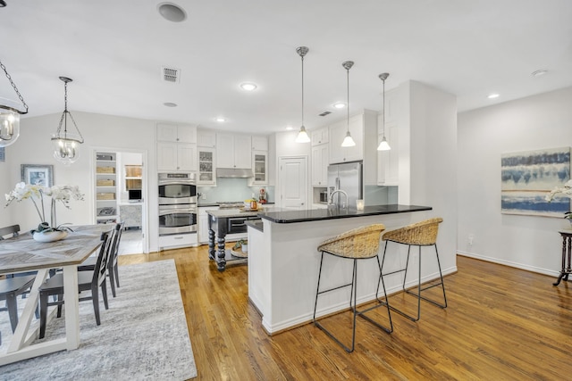 kitchen with visible vents, under cabinet range hood, a peninsula, appliances with stainless steel finishes, and white cabinets