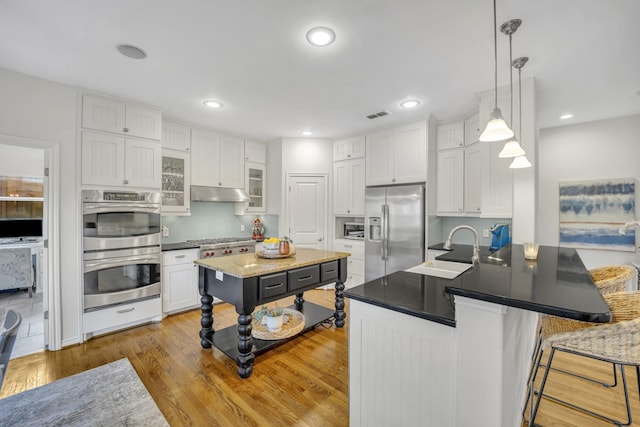 kitchen featuring visible vents, a sink, stainless steel appliances, under cabinet range hood, and white cabinetry