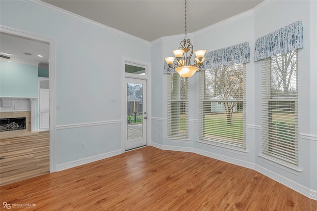 unfurnished dining area featuring a fireplace, crown molding, plenty of natural light, and wood finished floors