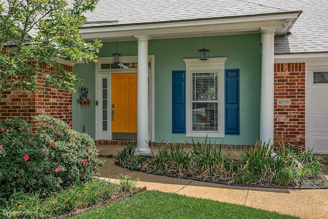 entrance to property with an attached garage, brick siding, and roof with shingles