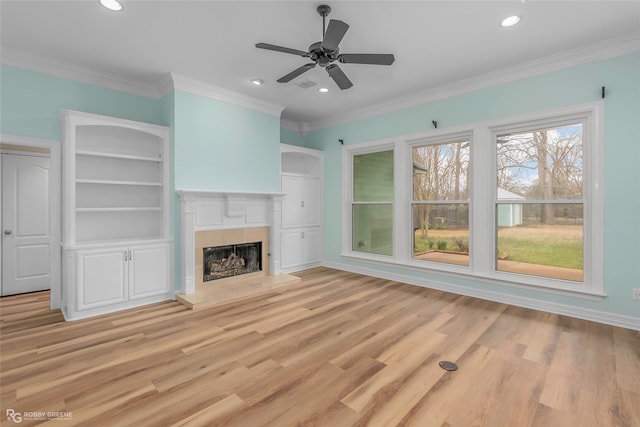 unfurnished living room with recessed lighting, a fireplace with raised hearth, crown molding, and light wood-type flooring