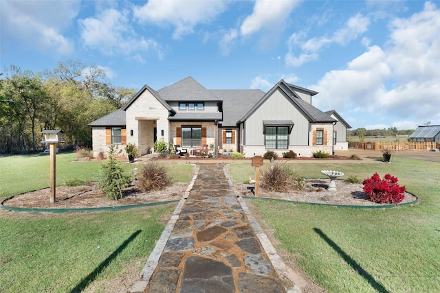 view of front facade featuring brick siding, board and batten siding, a front yard, and a shingled roof