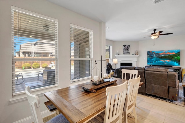 dining area with light tile patterned floors, visible vents, baseboards, a fireplace, and ceiling fan