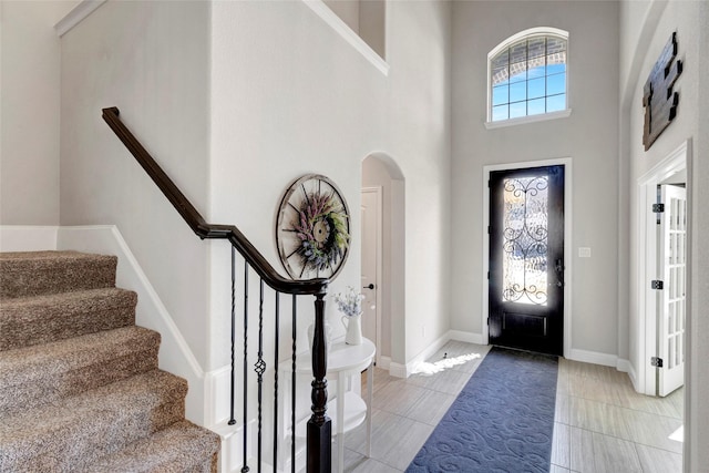 foyer featuring light tile patterned floors, baseboards, and a towering ceiling