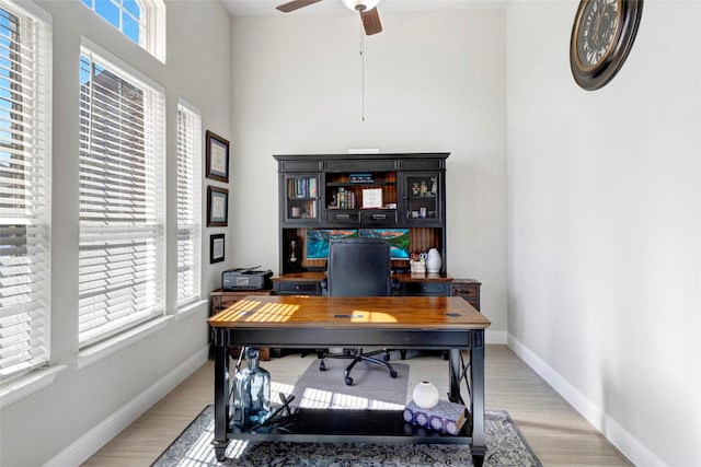 office area with light wood-style flooring, a ceiling fan, and baseboards