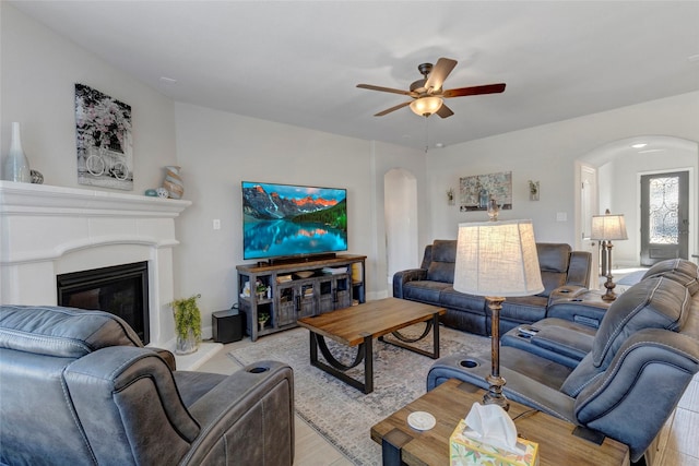 living area featuring arched walkways, a glass covered fireplace, light wood-style floors, and a ceiling fan