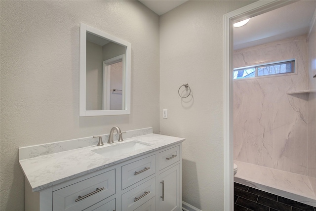 bathroom with toilet, walk in shower, vanity, and a textured wall