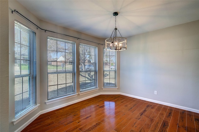 empty room featuring an inviting chandelier, baseboards, and hardwood / wood-style floors