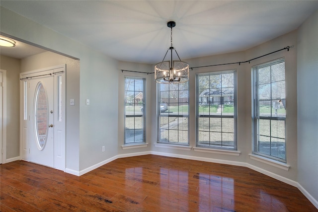 unfurnished dining area with dark wood-type flooring, a notable chandelier, and baseboards