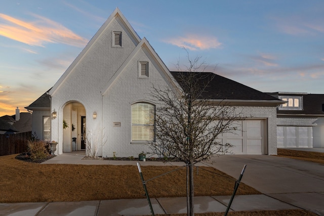 french country home featuring driveway, fence, roof with shingles, a garage, and brick siding