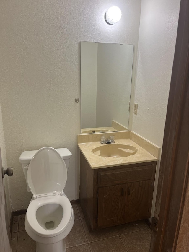 bathroom with tile patterned floors, toilet, vanity, and a textured wall