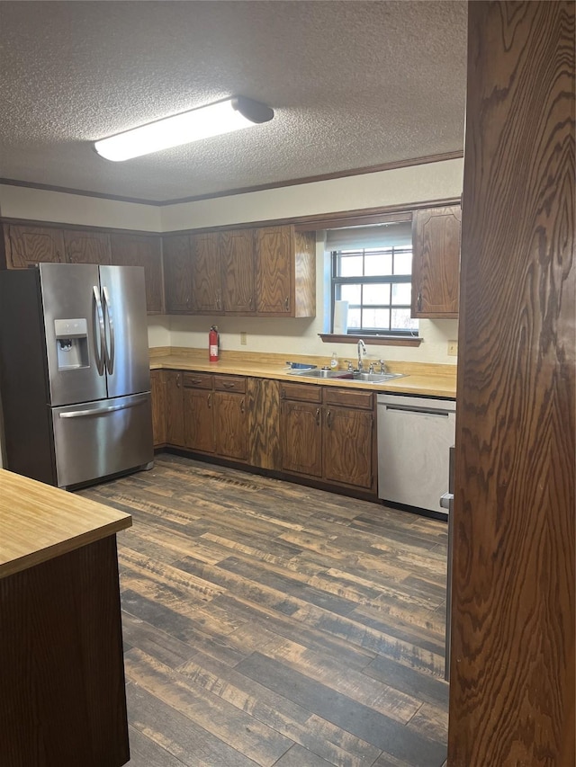 kitchen featuring dark brown cabinets, dark wood finished floors, appliances with stainless steel finishes, a textured ceiling, and a sink