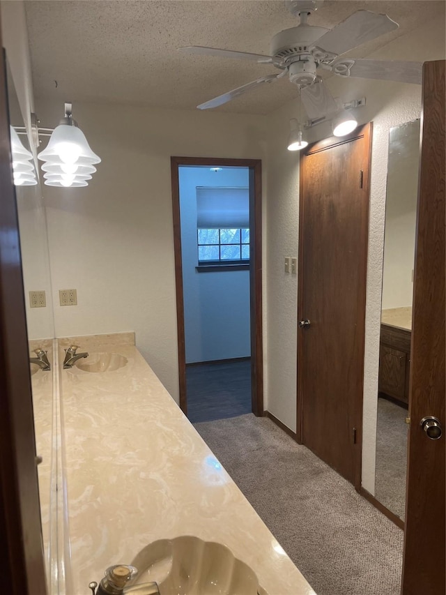 bathroom featuring vanity, ceiling fan, a textured wall, and a textured ceiling