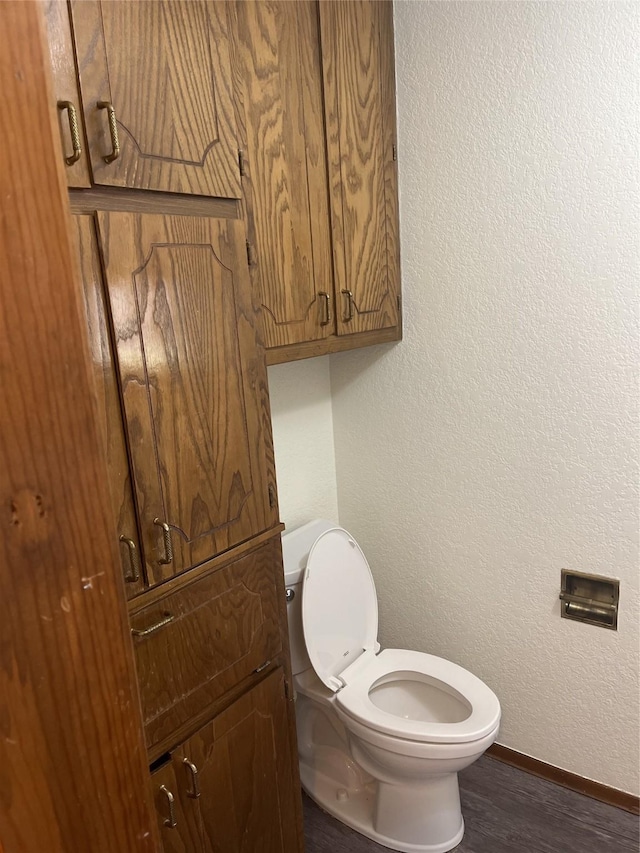 bathroom with baseboards, toilet, wood finished floors, and a textured wall