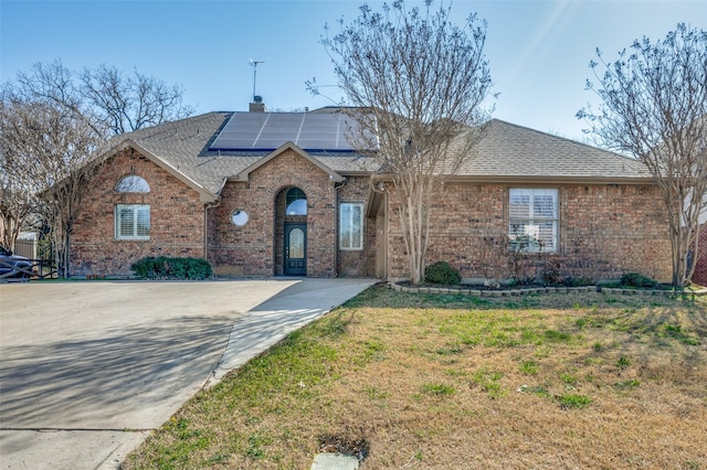 single story home featuring roof with shingles, solar panels, a chimney, a front lawn, and brick siding