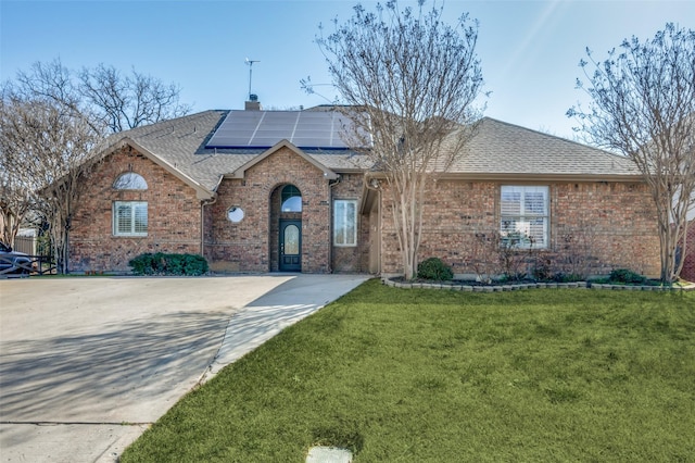 single story home featuring roof with shingles, solar panels, a chimney, a front lawn, and brick siding