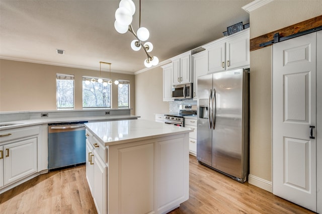 kitchen with a kitchen island, a barn door, ornamental molding, appliances with stainless steel finishes, and white cabinets