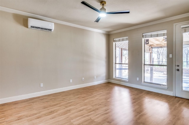 empty room featuring a wall mounted air conditioner, ornamental molding, a ceiling fan, light wood finished floors, and baseboards