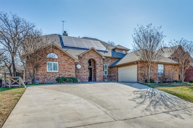 view of front of home featuring roof with shingles, an attached garage, concrete driveway, brick siding, and roof mounted solar panels