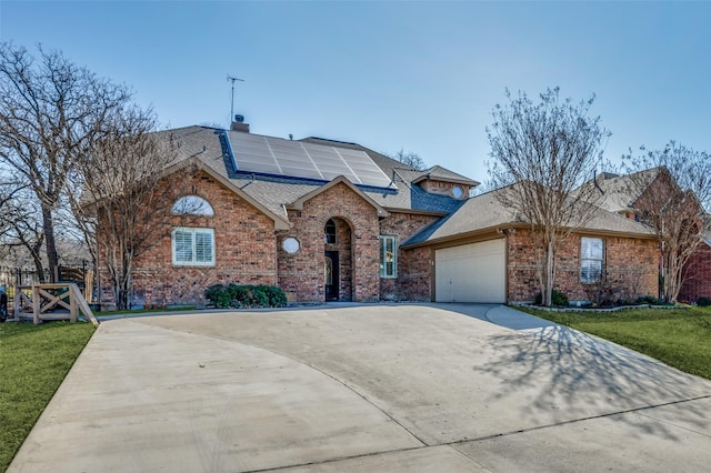 view of front of home featuring roof with shingles, an attached garage, concrete driveway, brick siding, and roof mounted solar panels