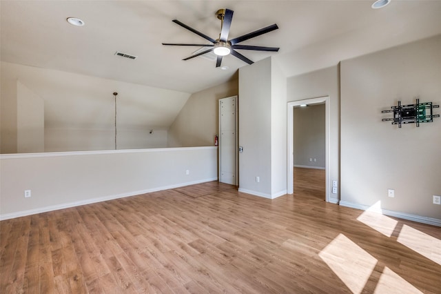 additional living space featuring visible vents, a ceiling fan, light wood-style floors, baseboards, and vaulted ceiling