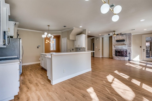 kitchen with stainless steel microwave, open floor plan, a stone fireplace, ceiling fan with notable chandelier, and white cabinetry