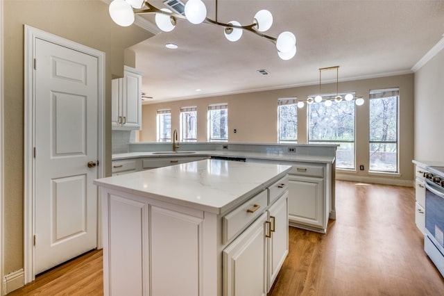 kitchen featuring light wood-type flooring, ornamental molding, a sink, a center island, and a peninsula