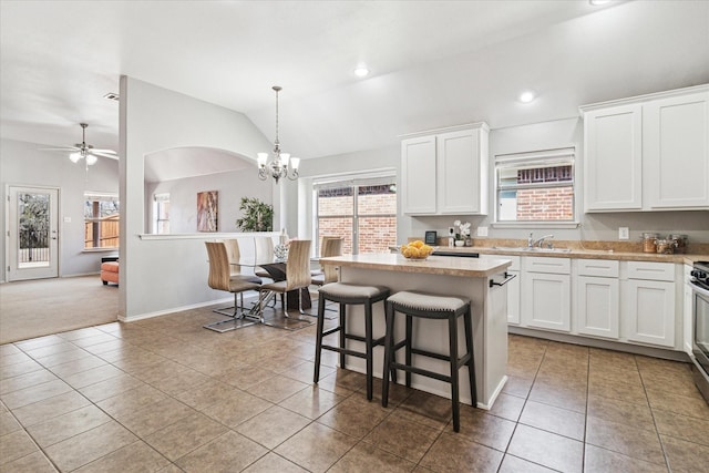 kitchen with a kitchen island, a sink, tile patterned flooring, vaulted ceiling, and light countertops