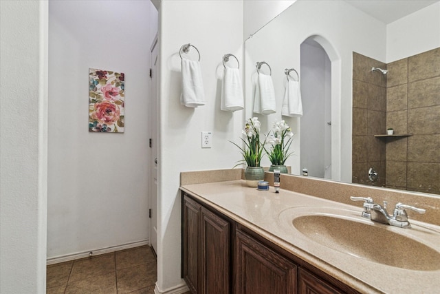 bathroom featuring tile patterned floors, tiled shower, vanity, and baseboards