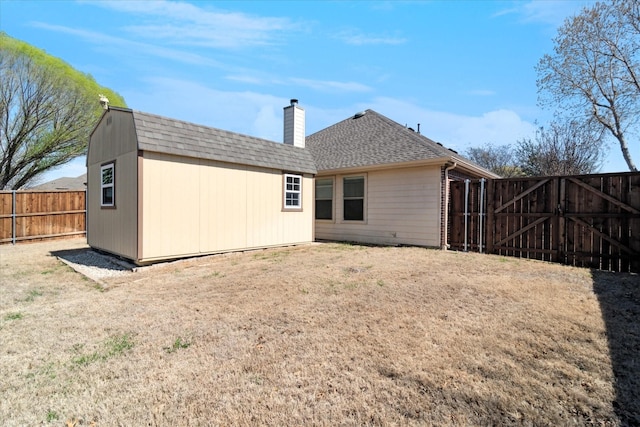 rear view of property with an outbuilding, a gate, a fenced backyard, a shingled roof, and a chimney