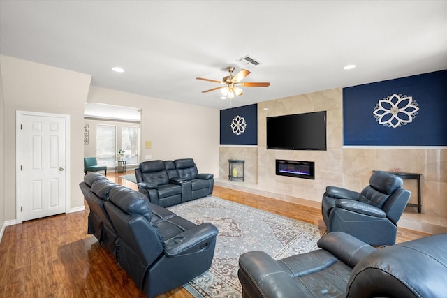 living area featuring visible vents, baseboards, ceiling fan, a premium fireplace, and wood finished floors