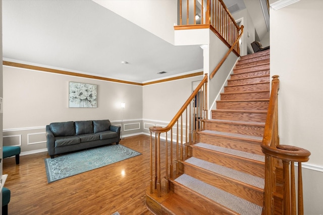 staircase featuring visible vents, a wainscoted wall, ornamental molding, wood finished floors, and a decorative wall