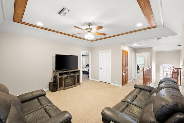 living area featuring a ceiling fan, visible vents, baseboards, a raised ceiling, and light colored carpet