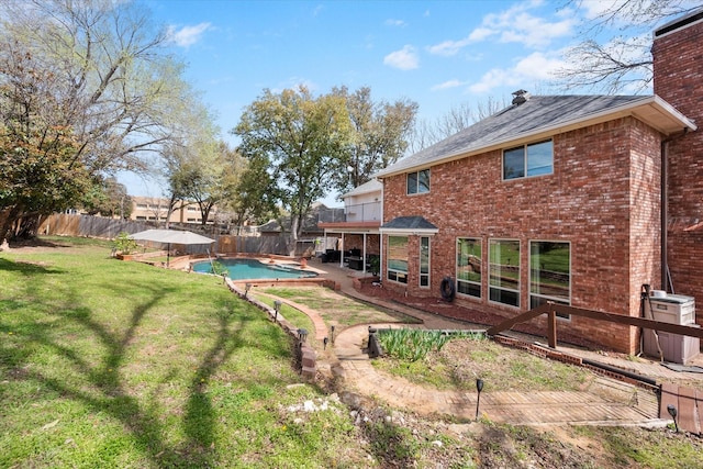 rear view of house featuring a fenced in pool, a fenced backyard, a chimney, a lawn, and brick siding