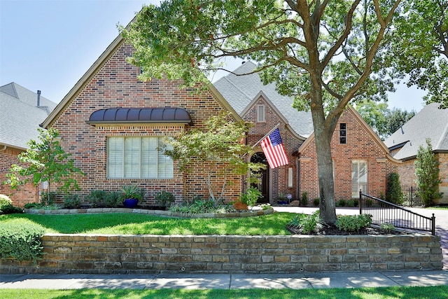 tudor home featuring a standing seam roof, brick siding, and a shingled roof