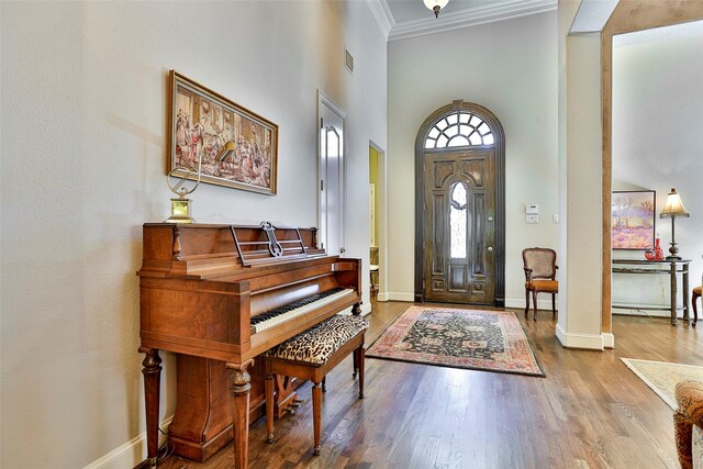 foyer entrance with visible vents, crown molding, baseboards, a towering ceiling, and wood finished floors