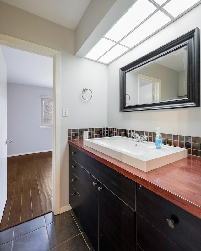 bathroom with tasteful backsplash, tile patterned flooring, vanity, and baseboards