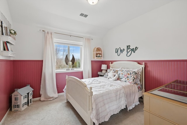 carpeted bedroom featuring a wainscoted wall, lofted ceiling, and visible vents