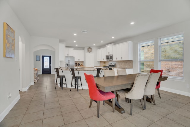 dining room with light tile patterned floors, baseboards, arched walkways, and recessed lighting