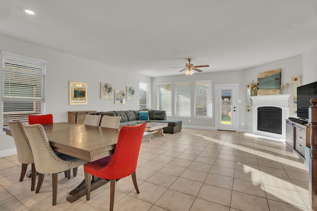 dining area with light tile patterned floors, a fireplace with raised hearth, a ceiling fan, and baseboards