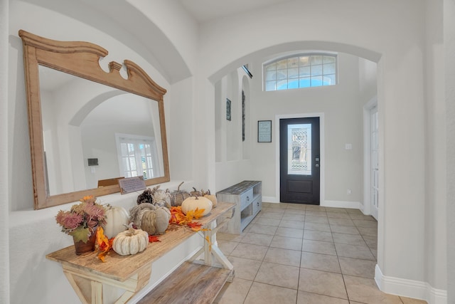 entryway featuring a high ceiling, light tile patterned floors, arched walkways, and baseboards