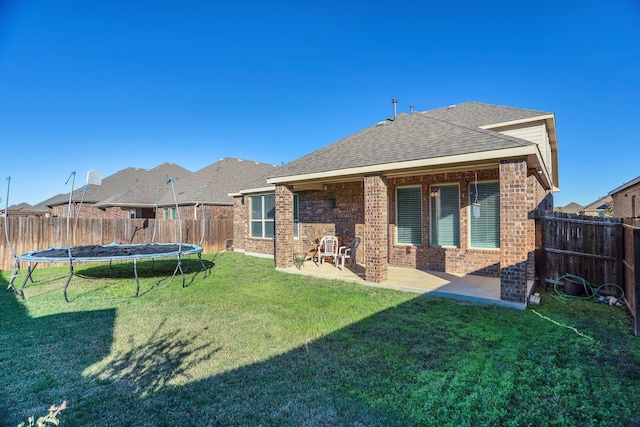 rear view of property featuring a patio, a fenced backyard, a trampoline, a lawn, and brick siding