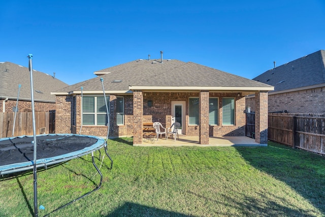 back of property with a trampoline, a fenced backyard, brick siding, and a lawn