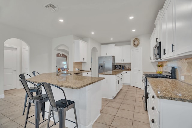 kitchen with visible vents, a sink, dark stone countertops, a kitchen island, and stainless steel appliances