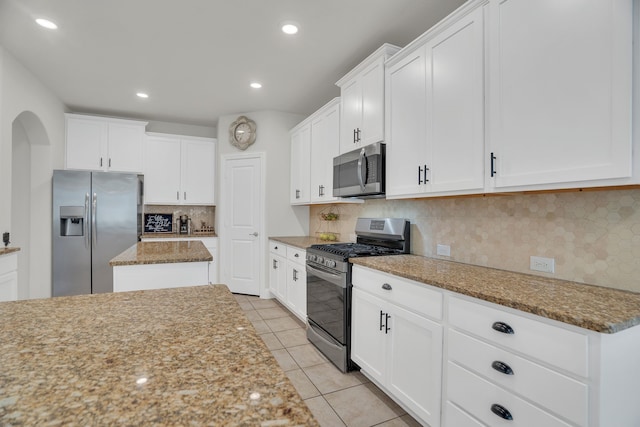 kitchen featuring light stone counters, light tile patterned flooring, white cabinets, appliances with stainless steel finishes, and tasteful backsplash