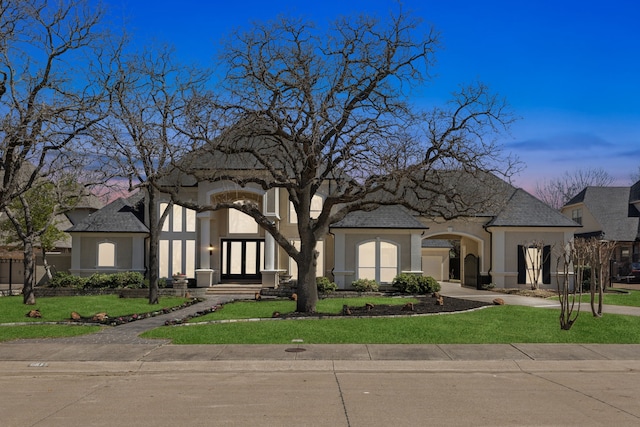 view of front of property with stucco siding, french doors, and a yard